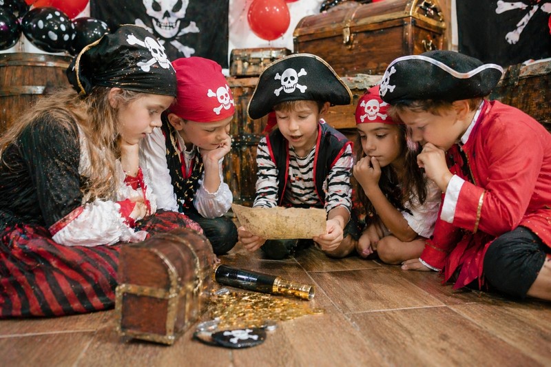Riddles for pirates aged 4–12 years 2 Children dressed as pirates sitting in a circle, solving riddles together at a pirate birthday party with treasure chest decorations