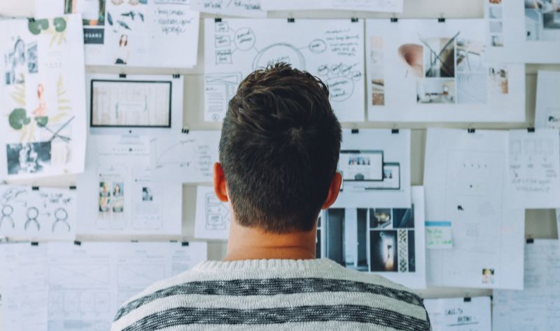 Man planning an adult scavenger hunt with a wall full of notes, sketches, and creative ideas