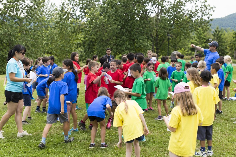 Large group birthday game: 20+ children doing a team scavenger hunt at a park or large backyard, split into colour-coded teams, adult facilitators